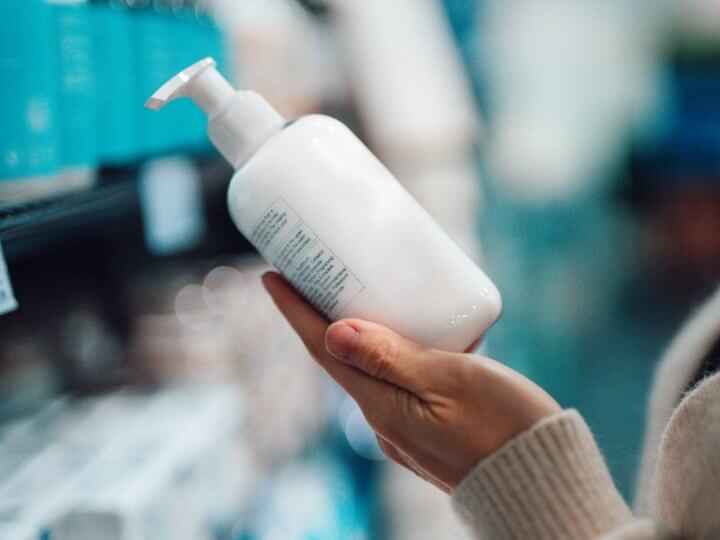a shopper in a supermarket holds up a clear plastic bottle containing a personal care product