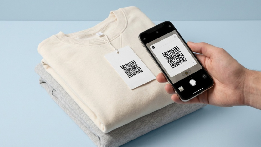 A comfy clothing displayed on a flat surface of a light blue color, a tag with QR code is attached to it. A phone is scanning the QR code on the tag.